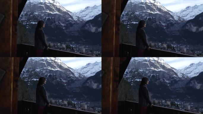 站在小屋阳台上欣赏山景的女人。冬季在瑞士阿尔卑斯山度假的人