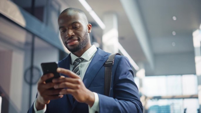 成功的非裔美国商人用智能手机站在办公楼里的肖像。黑人企业家使用手机电子商务应用程序进行股市投资活动。