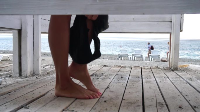 女人在海滩上的更衣间里，在日落的海边。女孩换了衣服，抛出了一件泳衣，然后穿着一件粉红色的裙子离开了更