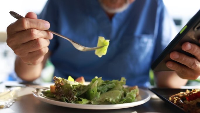 老年患者在食堂吃健康沙拉午餐，使用智能手机，健康生活方式。