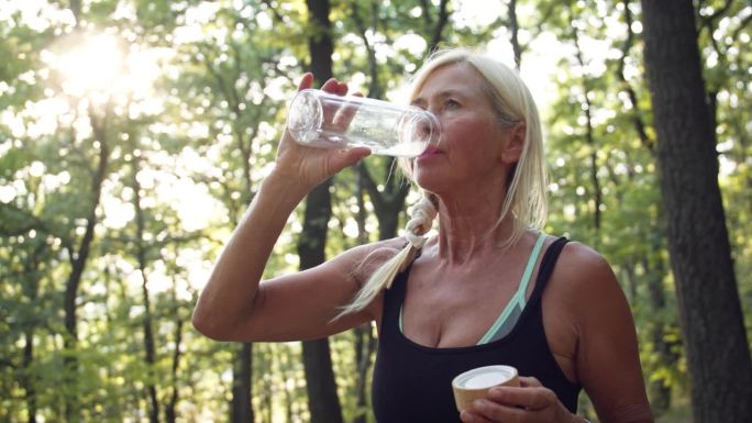 快乐活跃的老年妇女在森林休息时从可持续瓶中喝水。