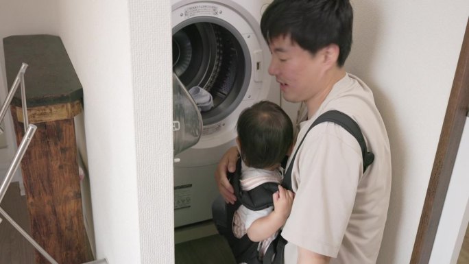 父亲抱着孩子洗完毛巾，从洗衣机里拿出毛巾。