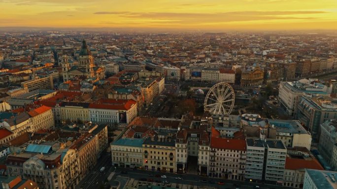 在日落时分，匈牙利布达佩斯拥挤的城市景观中，摩天轮和圣斯蒂芬大教堂的空中无人机镜头