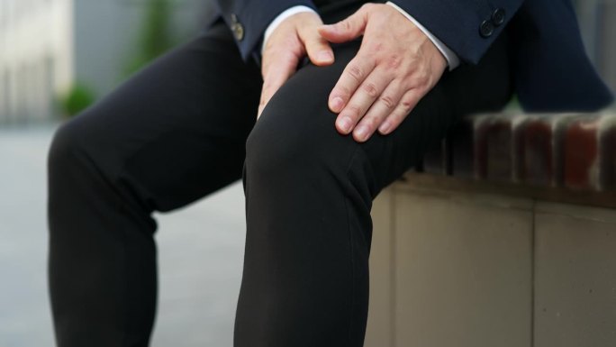 男性坐在街上的长椅上按摩膝盖和腿部肌肉。