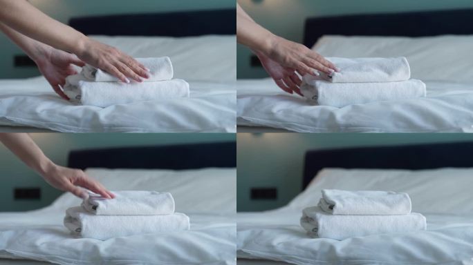 手把一叠干净的白色浴巾放在床单上的特写。客房服务员打扫酒店房间。