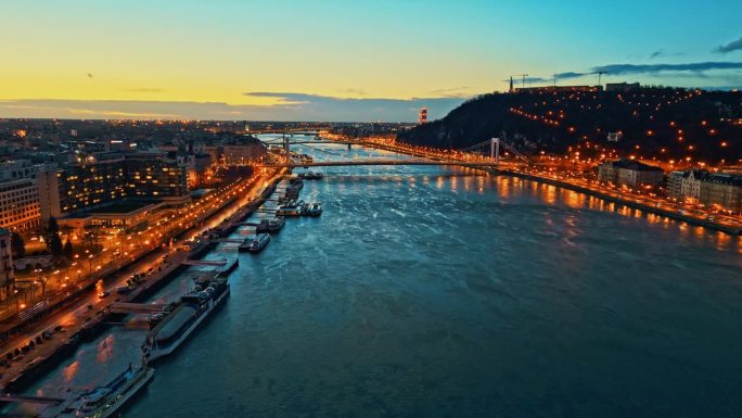 空中无人机拍摄的多瑙河在照亮城市景观在黄昏的天空，匈牙利布达佩斯