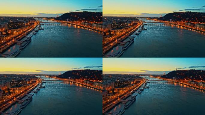 空中无人机拍摄的多瑙河在照亮城市景观在黄昏的天空，匈牙利布达佩斯