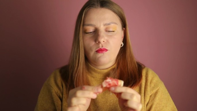 年轻女子喜欢吃熏火腿肉。她手里拿着三片，孤立在明亮的粉红色背景上，画室肖像。高质量的全高清镜头