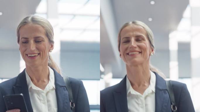 垂直屏幕:一个女人在使用她的智能手机，微笑着走在空荡荡的办公大厅里。一位穿着时髦休闲装的女商人，端着