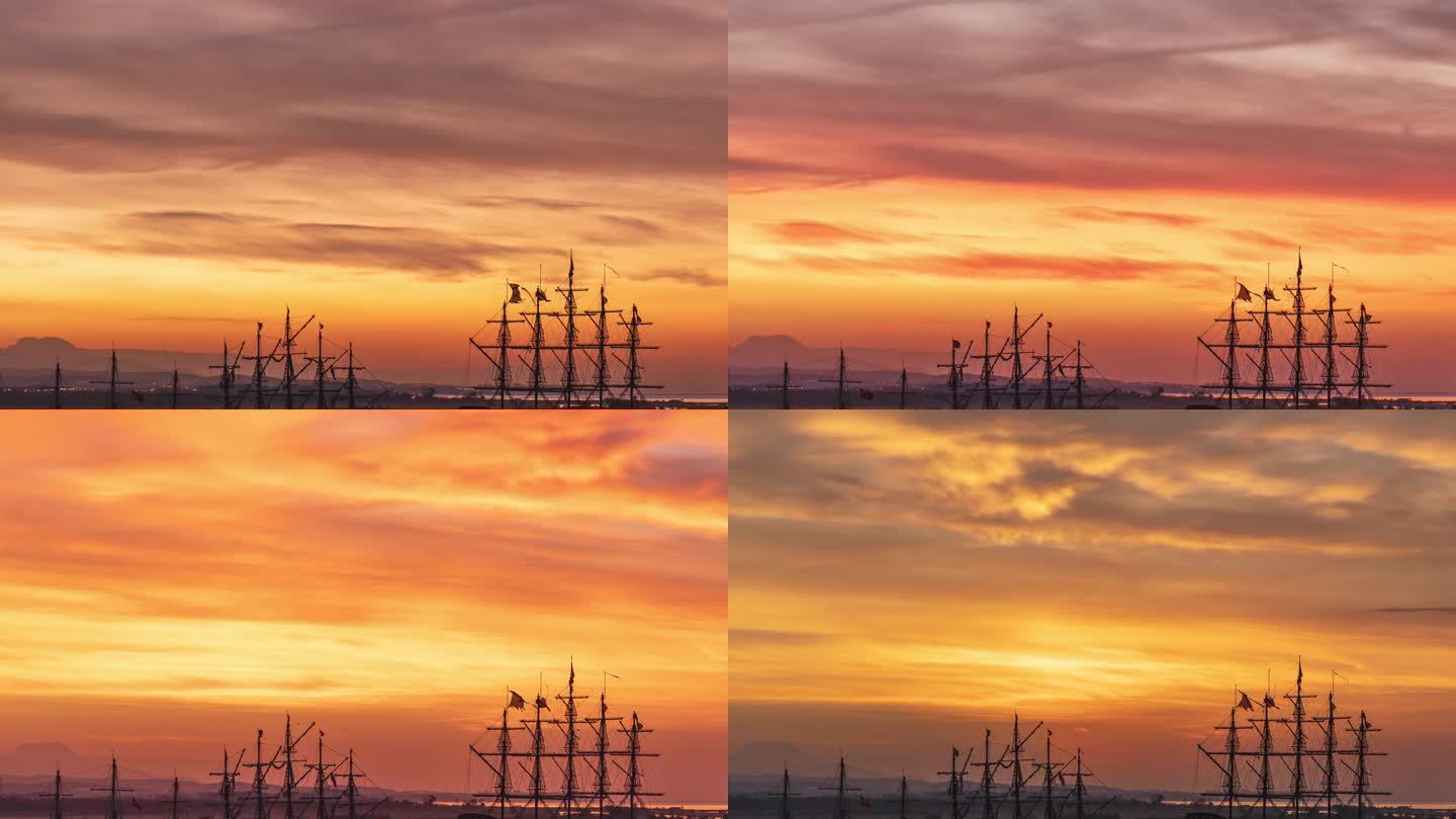 古老帆船的高桅杆和顶上展开的破烂旗帜，背景是冉冉升起的太阳和火红的云。延时。