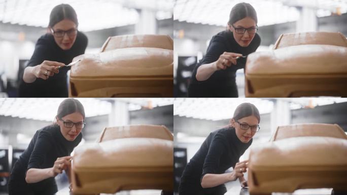 近距离肖像的汽车设计师雕刻一个新的生产汽车的3D粘土模型。年轻女性用抹刀小心地擦拭一辆概念车的表面