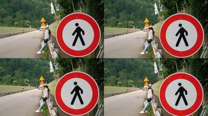 道路标志，圆形，中间有一个黑色的男人剪影和一个红色的框架，禁止行人通行。特写镜头。背景里有个女人。坐