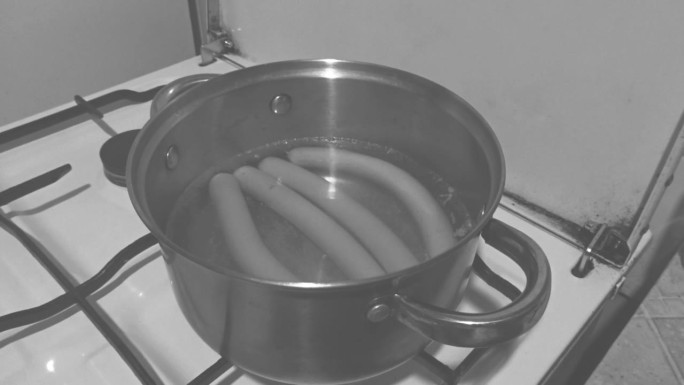 香肠在旧炉子上的锅里煮着，黑白相间的画面。