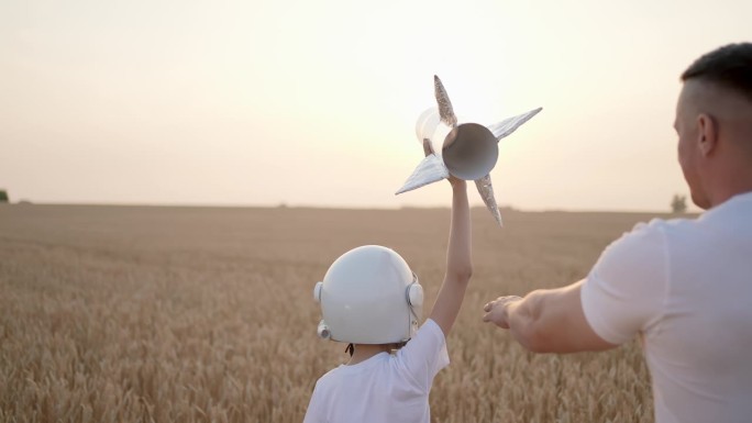 父亲、儿子、男孩、少年在日落的田野里玩着玩具火箭的飞行员、宇航员。孩子大梦想飞行宇航员空间，概念童年