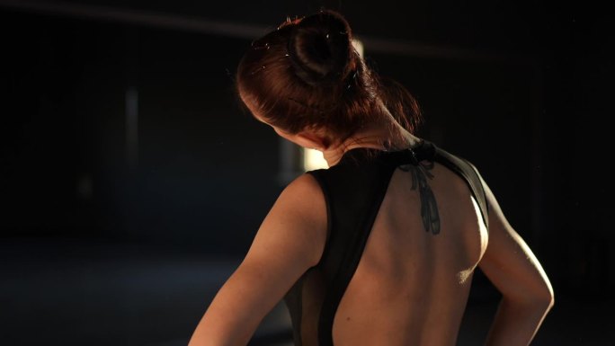 一名女子站在舞蹈教室的镜子前转动她的头，让她的颈部肌肉热身。