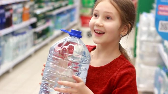 一个小女孩在商店里拿着装在一个5升大塑料瓶里的水。白种人女孩喝水。购买水