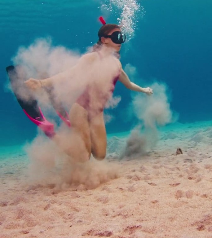 一名身穿粉色潜水服的女子在水下吹泡泡，享受着在热带海洋中游泳的乐趣