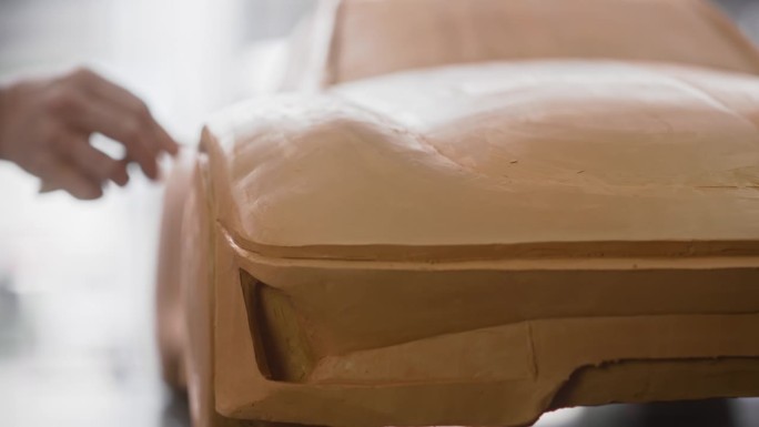 近距离的汽车设计师雕刻一个新的生产汽车的3D粘土模型。专业建模师使用抹刀仔细地光滑的原型可持续车辆的