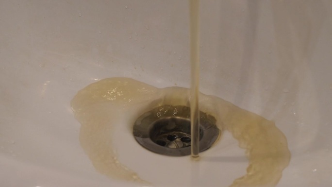 肮脏的生锈的水涌入家里浴室的水槽。紧急供水，脏水从水龙头流出特写。环境灾难