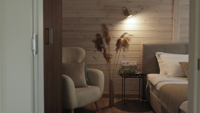 舒适的卧室，柔软的椅子，床，温暖的灯在木墙上。潘帕斯草原的草在高高的花瓶里作为室内装饰，舒适的房间在