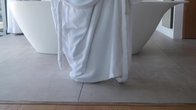 穿着浴袍的女人站在浴室里，腿的特写。