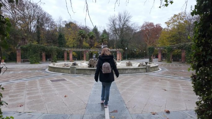 女游客漫步在公园的林荫道上，欣赏着巴利亚多利德喷泉，