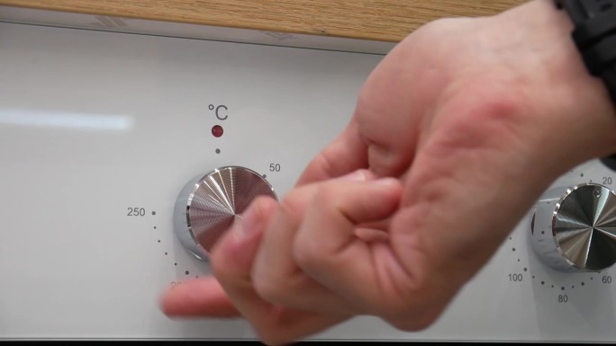 特写:一只男性的手转动烤箱的钢旋钮来打开烤箱