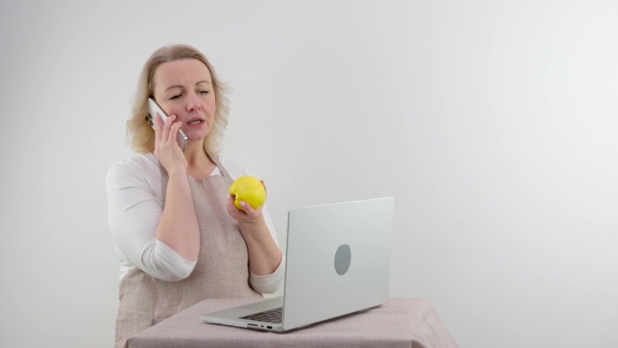 一个成熟的美丽的幸福的女人微笑诱人地讲电话拿着苹果家庭主妇健康饮食节食技术呼叫移动载体概念。