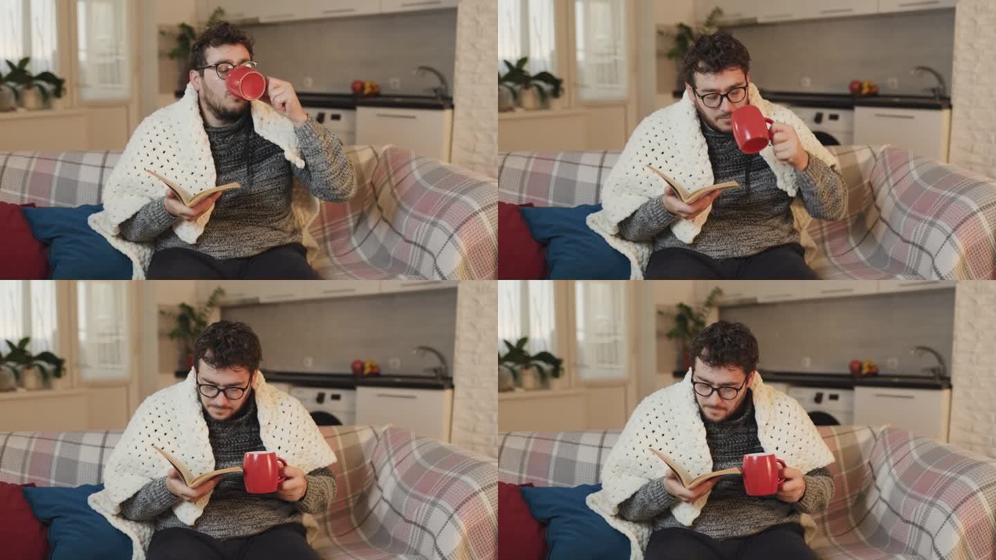 一个戴眼镜的男人一边用杯子喝药，一边在羽绒被下面看书