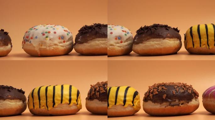 镜头在橙色背景上沿着不同口味和颜色的甜甜圈移动。