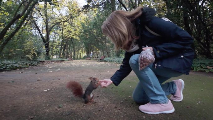 在西班牙巴利亚多利德的格兰德公园，一名妇女正在给松鼠喂坚果。