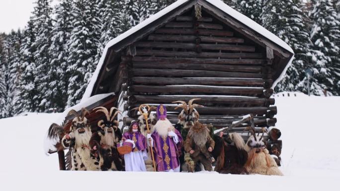 一群传说中的圣诞民间人物——圣尼古拉斯、天使和抽筋——站在一间木屋附近，背景是奥地利一座山上的云杉林