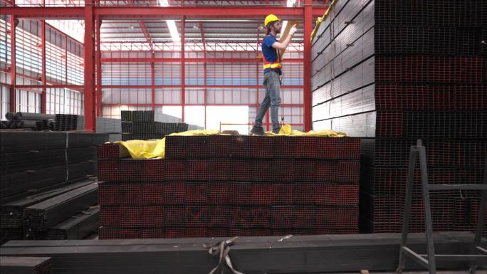 戴安全帽和安全帽的仓库工人站在仓库内清点和检查仓库内的钢材。
