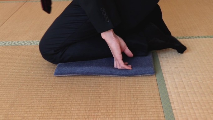 在铺着榻榻米的日式房间里，一名西装革履的男子坐在垫子上