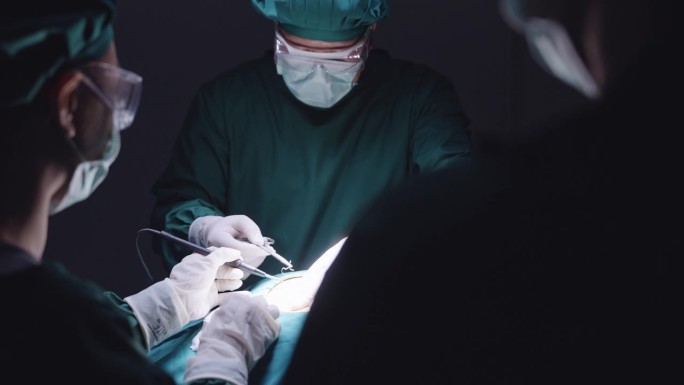 后视图，在腹部手术中，一名护士和一名助手站在一名外科医生的对面，后者正在对病人进行手术缝合。