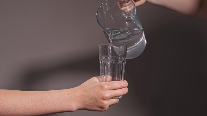 画框里的两只手拿着一个醒酒器和一个玻璃杯。装在一瓶干净的饮用水里。把水倒进杯子里。喝的政权。饮用水