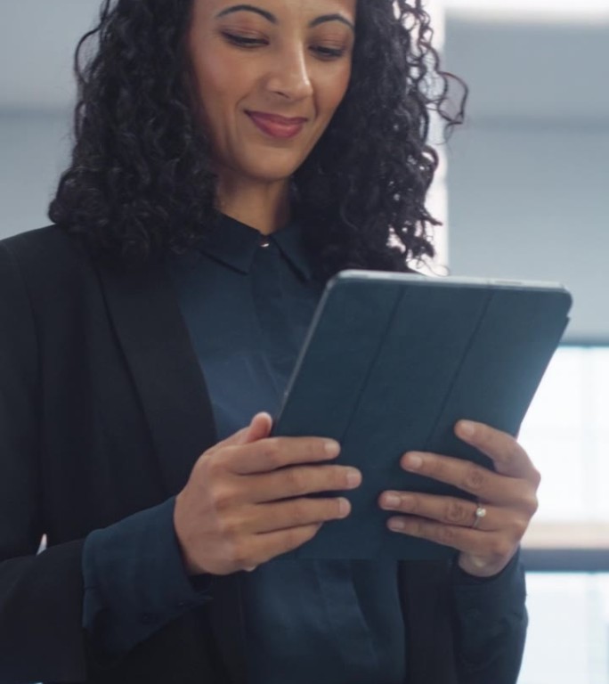 垂直屏幕:女性数据分析师微笑着检查当天的数字平板电脑上的新数据。自信的女商人走向公司大楼里的办公室