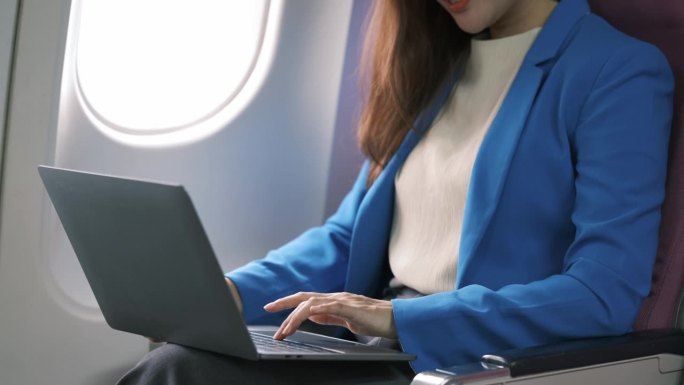亚洲年轻女性坐在飞机头等舱靠窗的位置使用笔记本电脑，旅游和商务概念