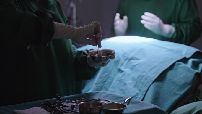 手术室里，一名护士用镊子夹住棉球，用聚维酮碘浸泡在病人的手术伤口上擦拭消毒。
