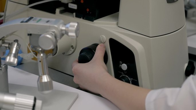 医学实验室技术员转动显微镜上的旋钮来调整焦距
