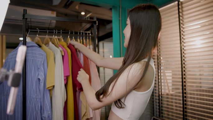 年轻的亚洲女性在办公室用手机直播教学视频，通过互联网在社交网络上销售一件衣服
