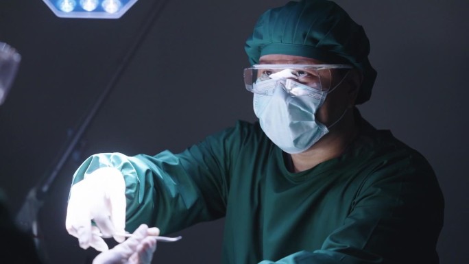 一名男性外科医生将镊子递给护士，并与他的团队交谈，他对手术成功后的结果感到满意。