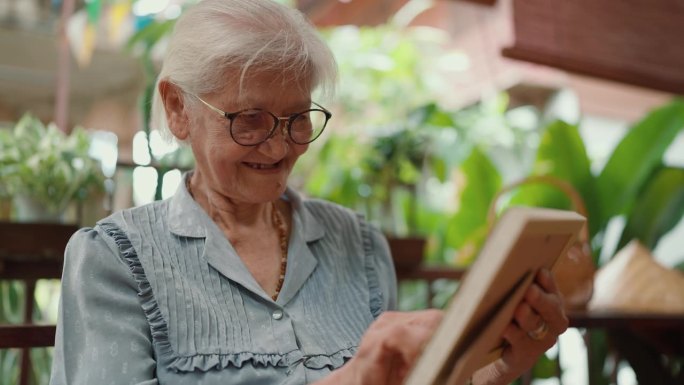 亚洲上了年纪的老奶奶在家里放松时看着家人的照片。慈爱的老祖母。老年人老年生活方式，老年人休闲理念