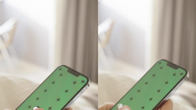 垂直视频。有绿屏模型和跟踪标记的智能手机，一个女人坐在白色的床上刷着社交媒体。