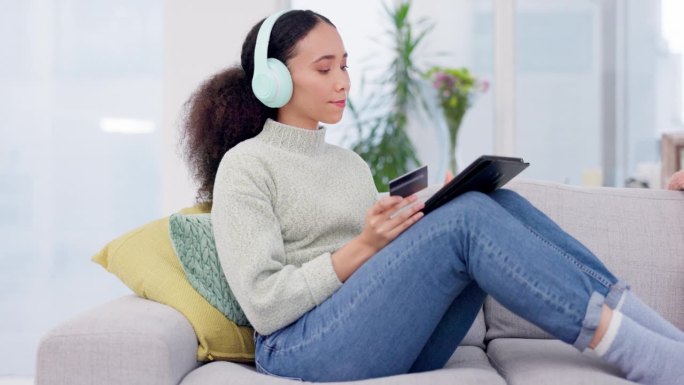 女人把耳机和信用卡放在平板电脑和沙发上，用于音乐流媒体订阅、电子商务或网上购物。年轻的非洲人对数字技