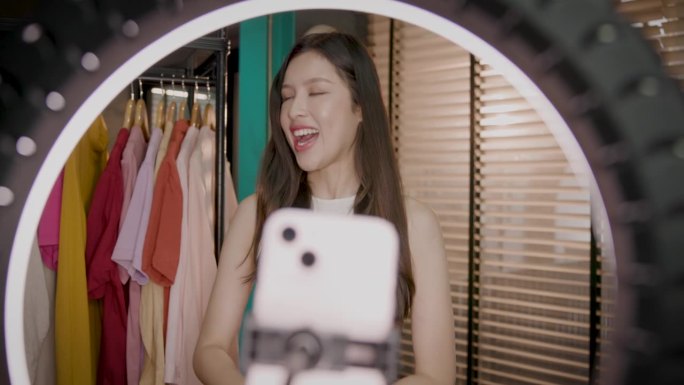年轻的亚洲女性在办公室用手机直播教学视频，通过互联网在社交网络上销售一件衣服