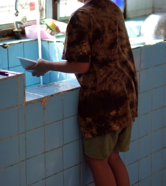 一个小孩子在厨房里帮妈妈洗碗的垂直视频片段。