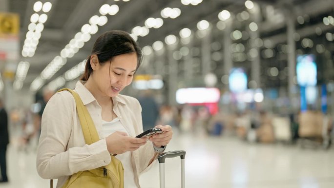 微笑的年轻亚洲女子在机场使用智能手机