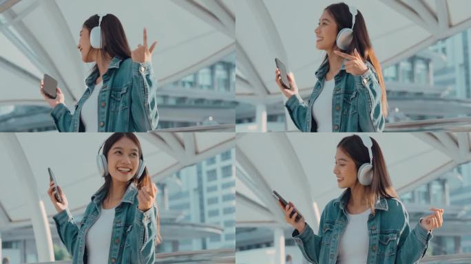 年轻的亚洲女子用耳机听好听的音乐，站在城市里。女孩幸福，笑脸迎人。女性喜欢听让她放松和享受生活的音乐