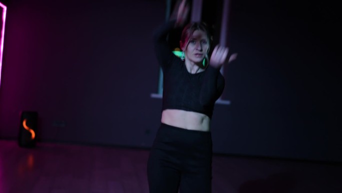 住相机。在霓虹灯下的舞蹈大厅里跳舞的女人。在表演舞蹈时积极地挥动手臂和手势。
